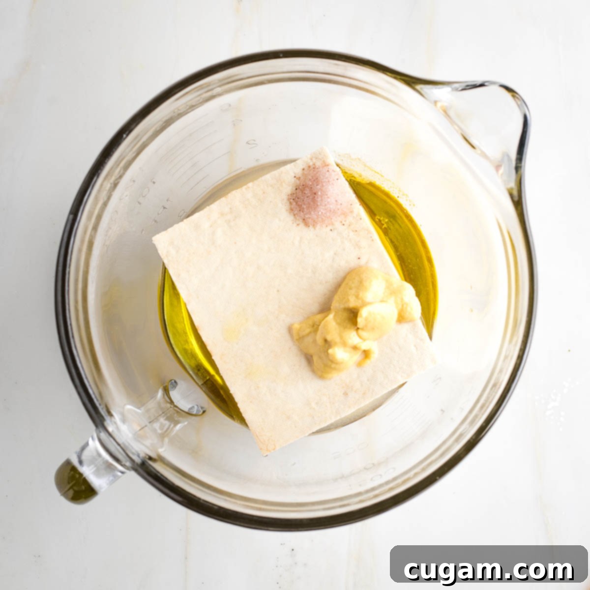 Large glass measuring cup with oil, vinegar, tofu, mustard and salt. 