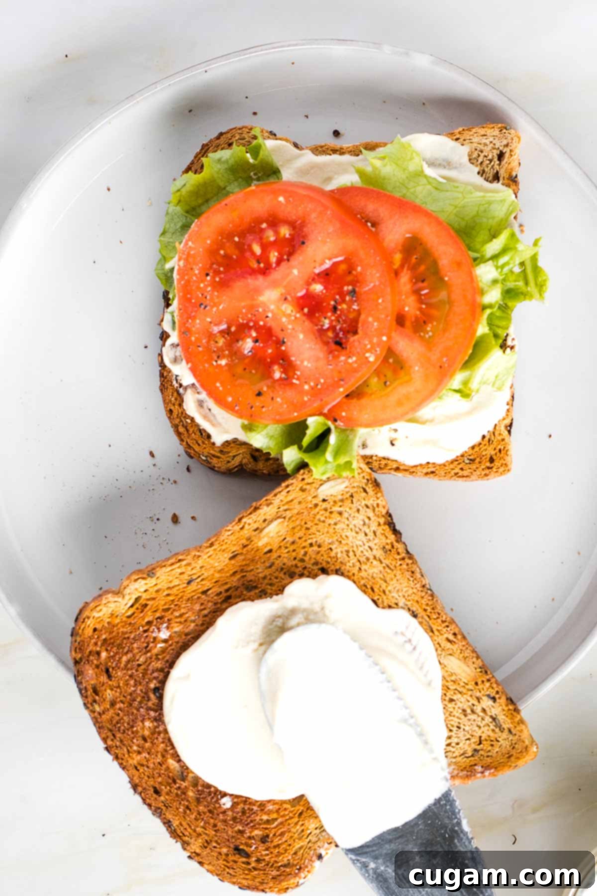 Vegan Mayo slathered on thick to a piece of toast, the other side has lettuce tomato slices and more mayonnaise.