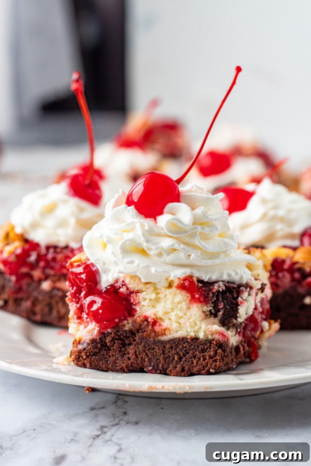 Cooked slice of cherry cheesecake brownie with whipped cream and cherry on white plate, ready to be enjoyed.