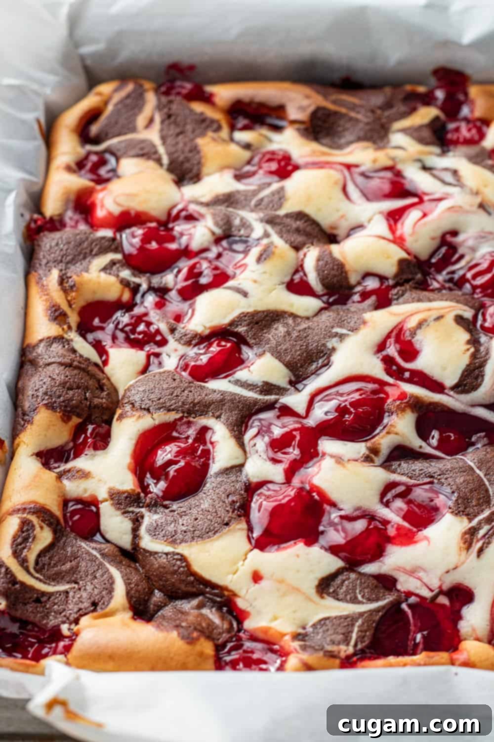 Baked cherry cheesecake brownies in a square pan lined with parchment paper, perfectly set and ready for cooling.
