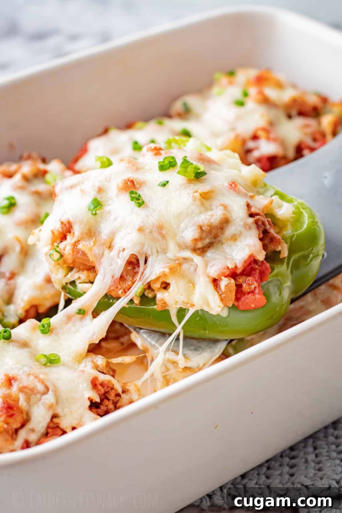 Ground Beef Stuffed Peppers: A healthy, cheesy recipe with beef, tomatoes, pinto beans, rice, and mozzarella. Baked ground beef stuffed pepper with melted cheese over white pan, showcasing a delicious, healthy dinner option.