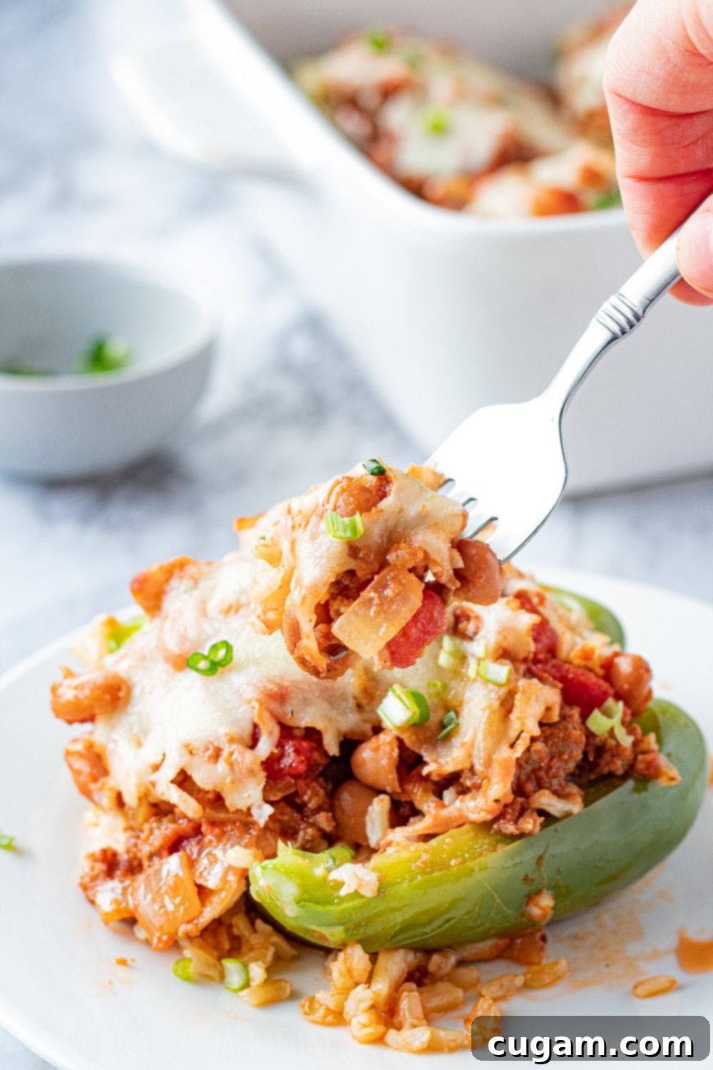 Ground Beef Stuffed Peppers: a healthy, cheesy, and satisfying family dinner. Cooked ground beef stuffed pepper with cheese on top with fork on a white plate, ready to be enjoyed.