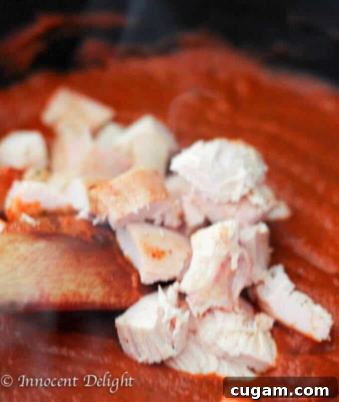 Adding cooked chicken pieces to the creamy tomato basil sauce.