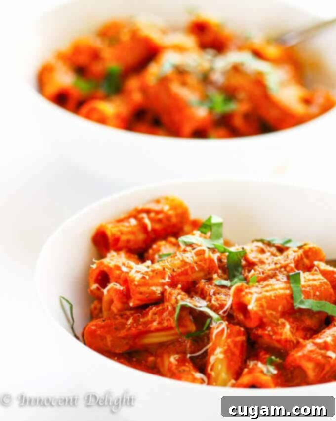 A large serving of Chicken Tomato Basil Rigatoni in a rustic white bowl, topped with basil.