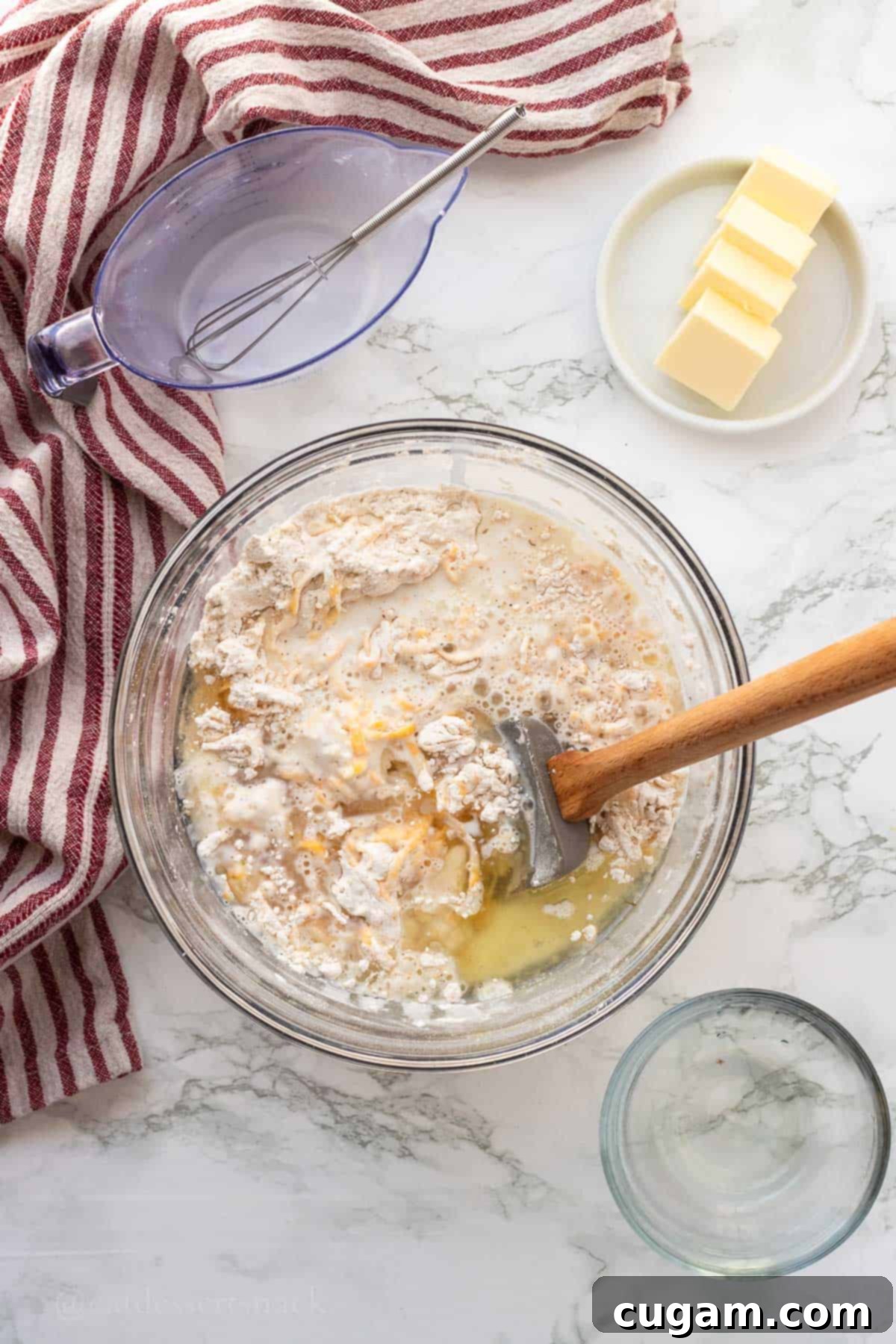 Wet and dry ingredients for biscuits in glass bowl with spatula.