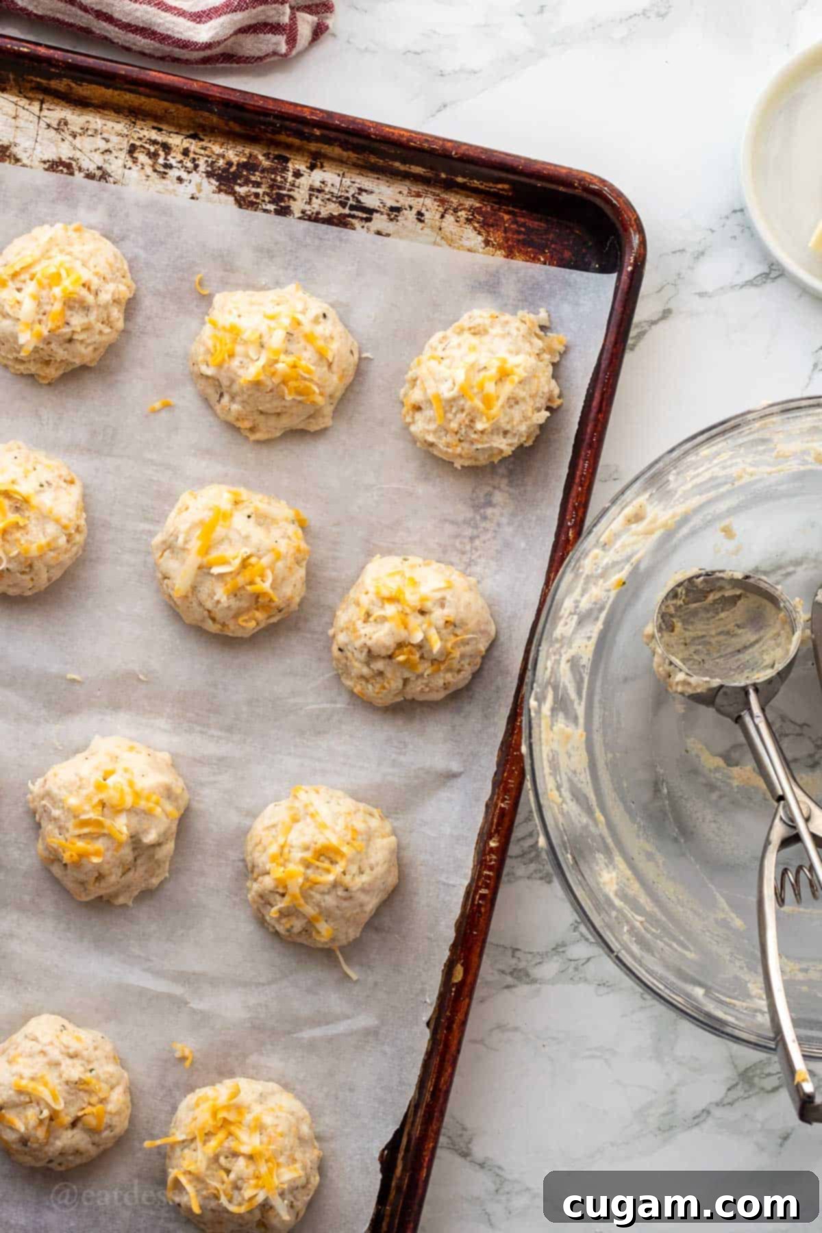 Raw garlic cheese biscuit dough balls on parchment paper on metal baking sheet.