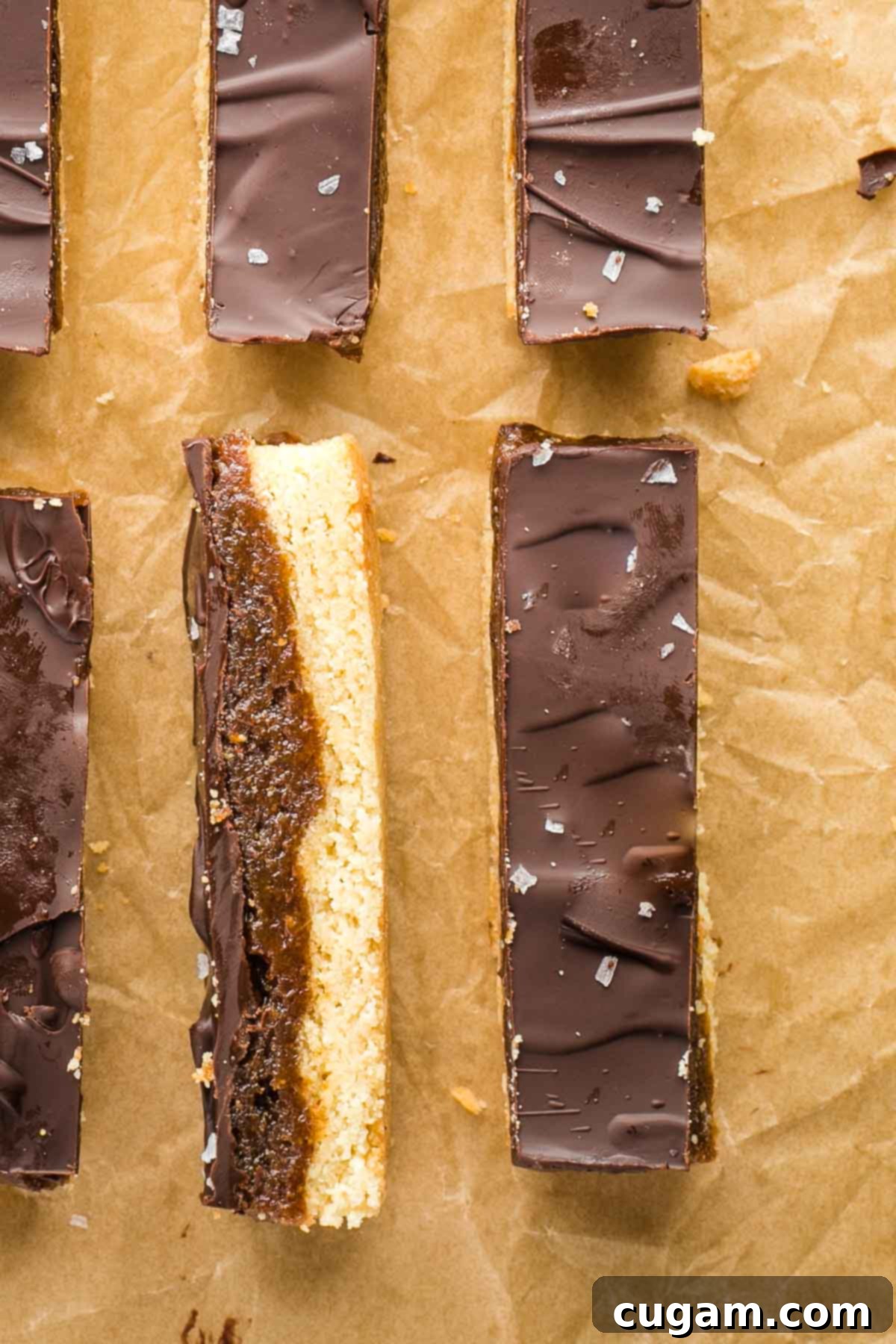 Homemade twix bars shown with a sprinkle of flakey sea salt, one turned on its side so you can see the three layers.