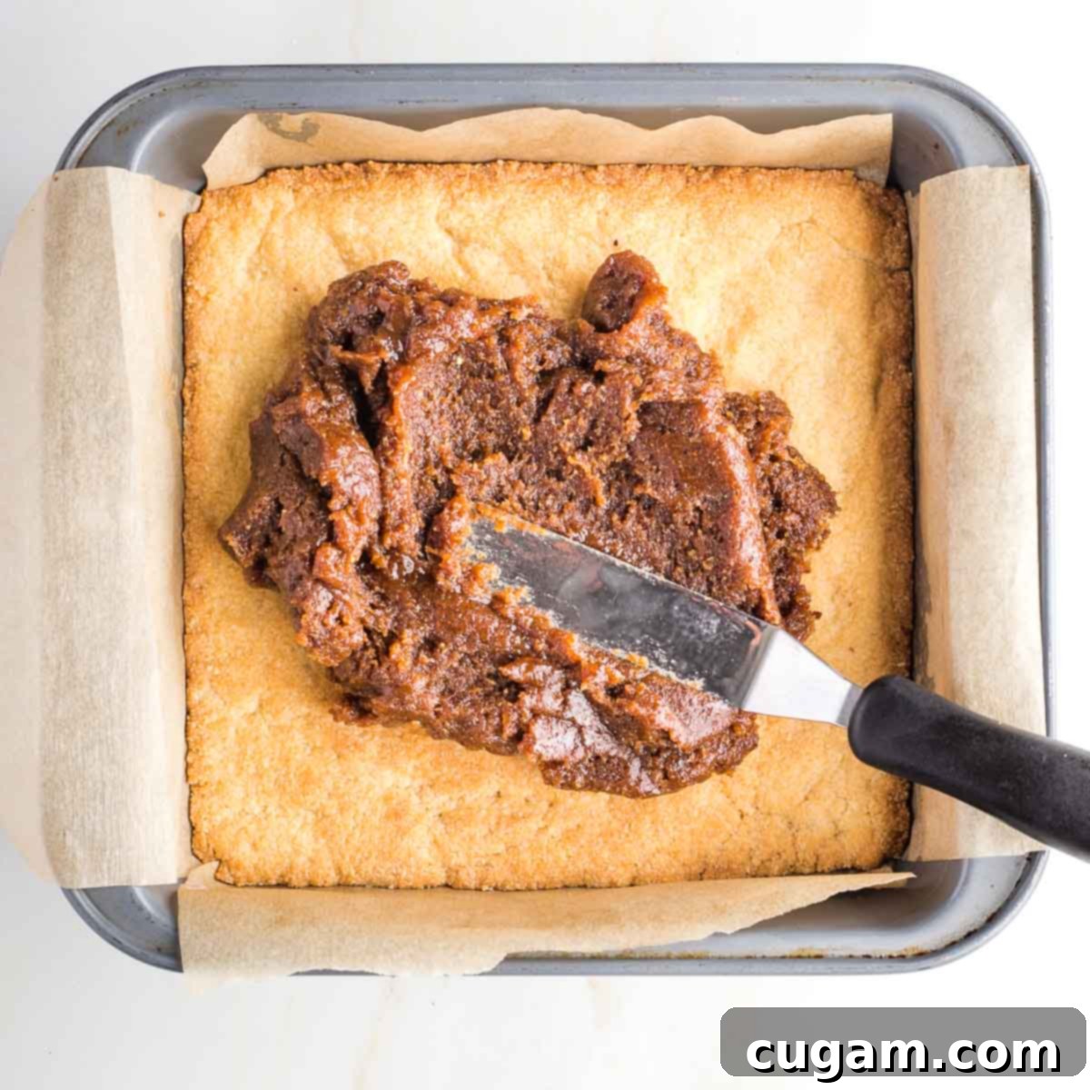 Thick caramel on top of a cookie layer in a square baking pan.