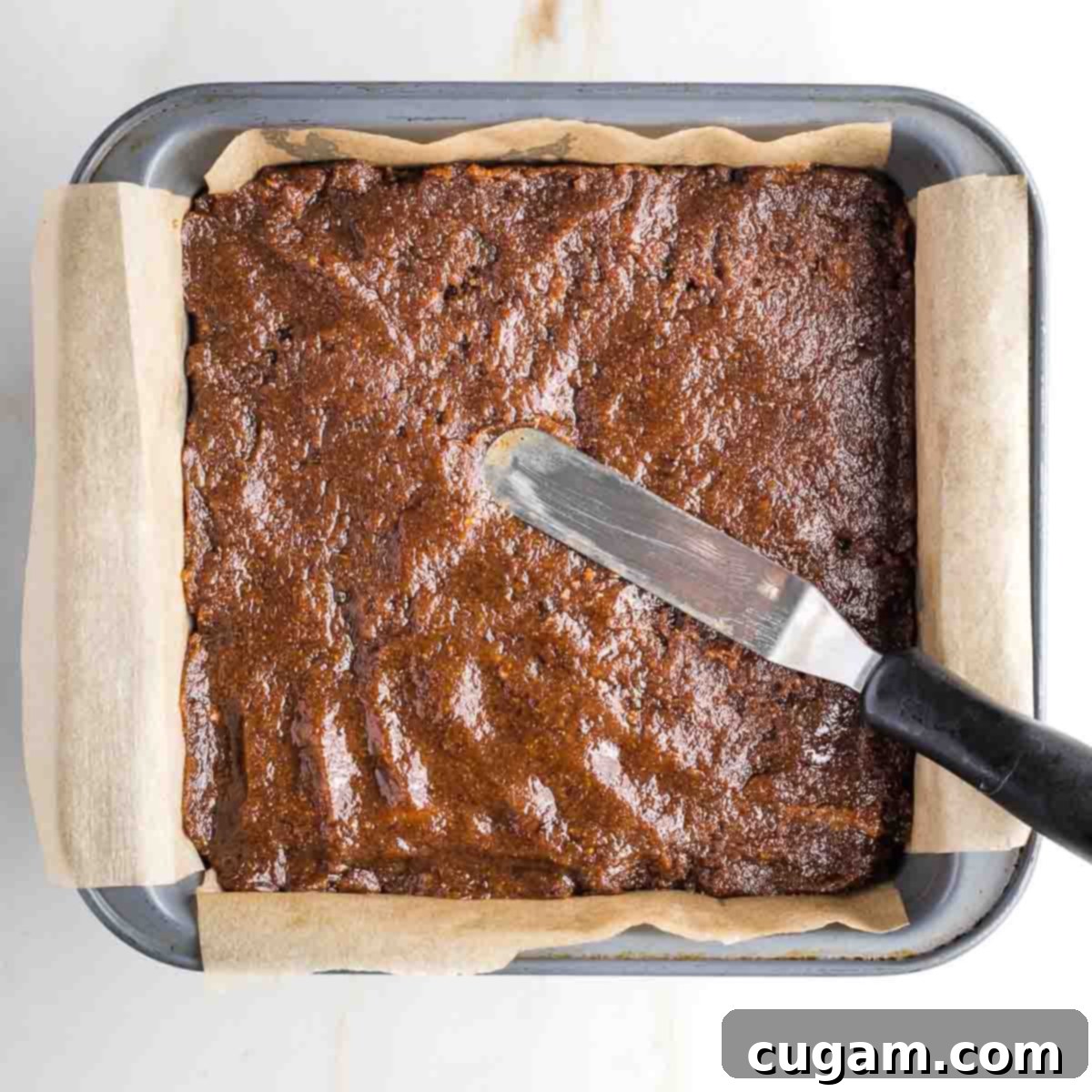 Offset spatula spreading caramel onto a thin biscuit cookie base.
