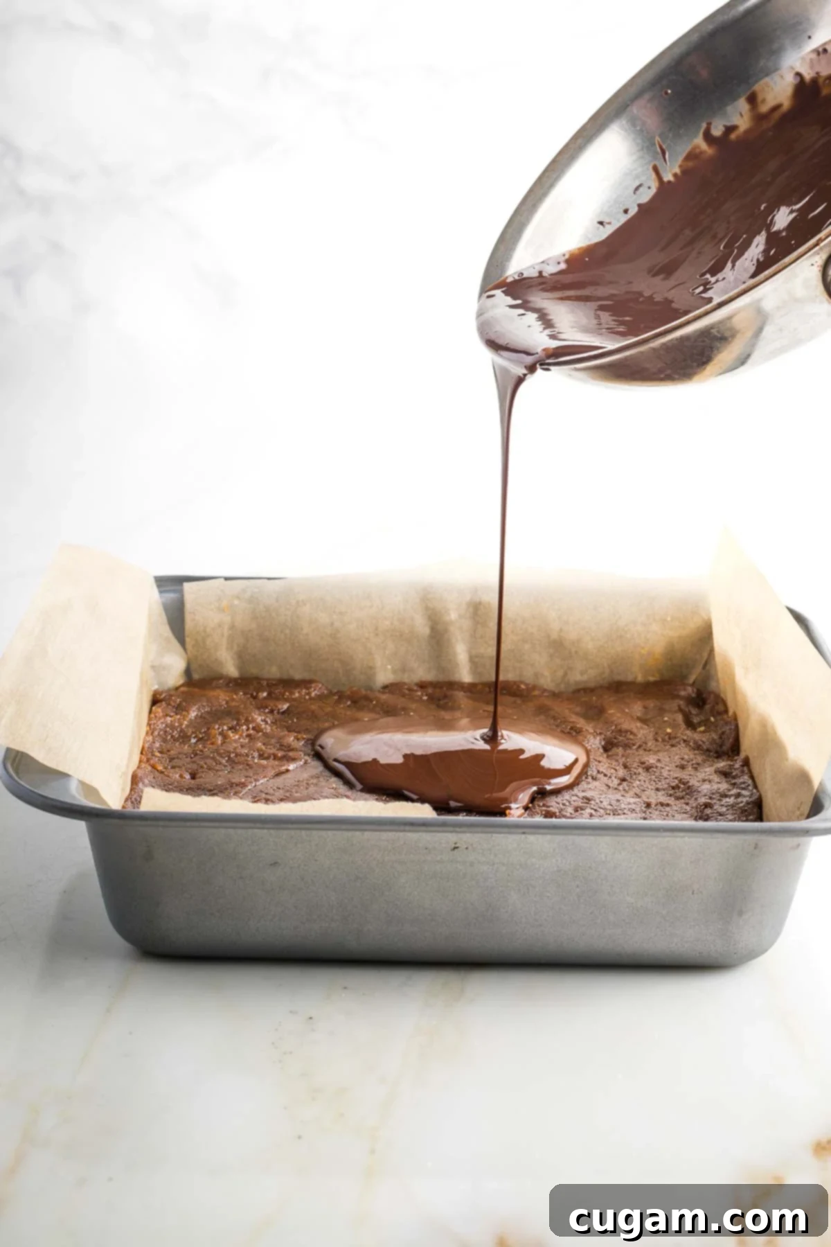 Melted chocolate poured from a small pan onto baked goods in a square baking pan.