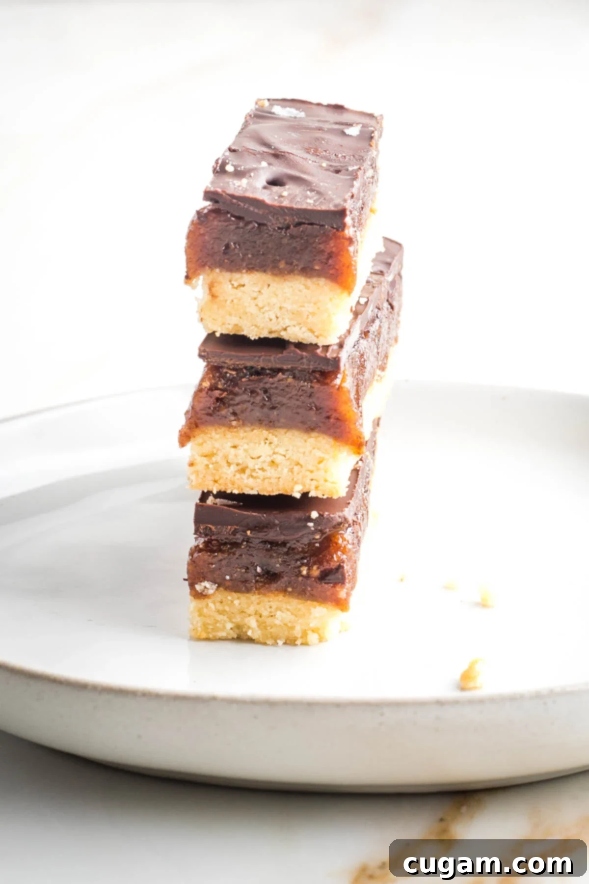 Three homemade twix bars stacked on top of each other. You can see the three layers: cookie, caramel and chocolate on the side.