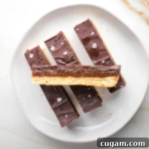 Three homemade twix bars lined up on a plate with one turned sideways across the top so you can see the three layers.