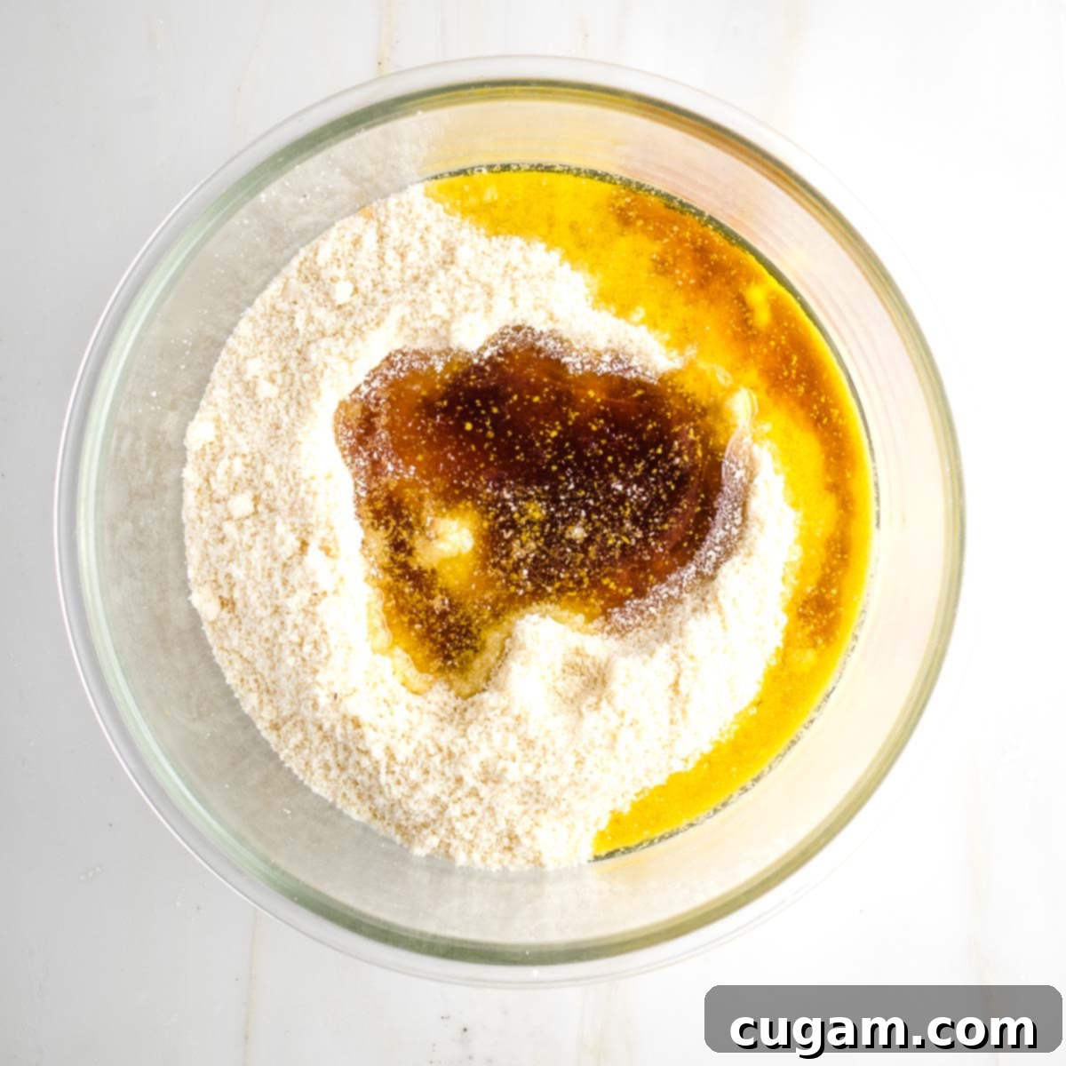 Almond flour in a mixing bowl along with olive oil and maple syrup.
