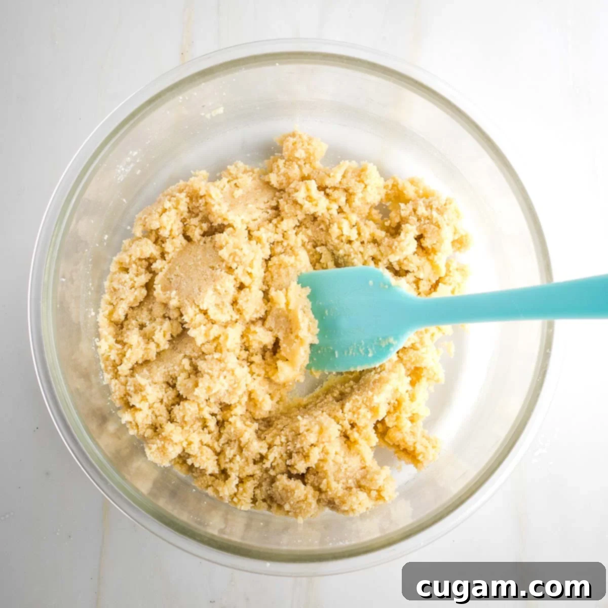 Cookie dough in a glass mixing bowl with aqua colored silicone spatula.