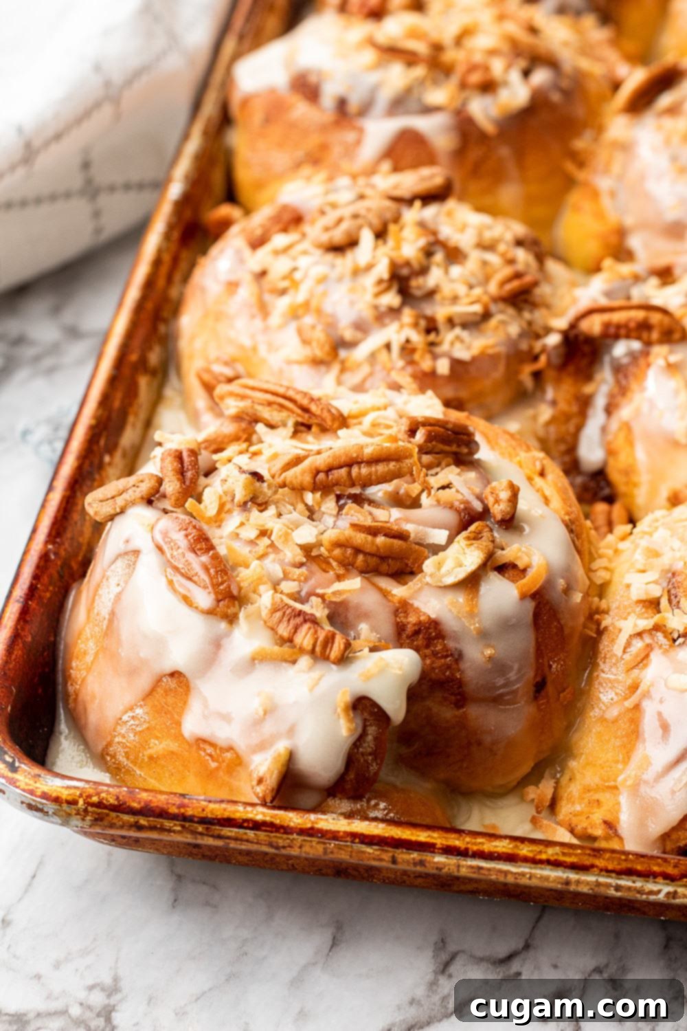 Baked carrot cake cinnamon roll with pecans and coconut on top in a metal pan on marble.