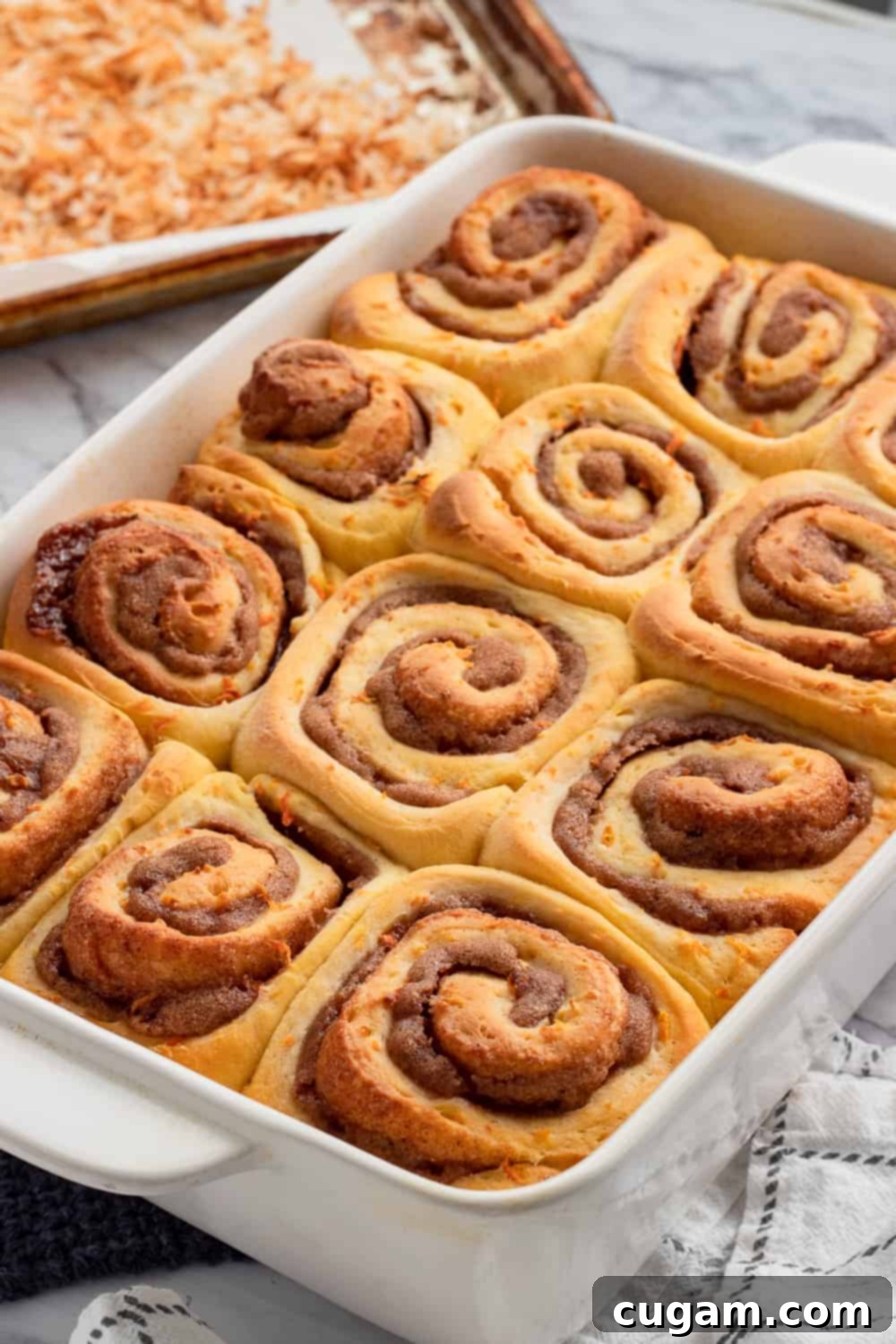 Baked carrot cake cinnamon rolls in white pan on marble counter with toasted coconut. 