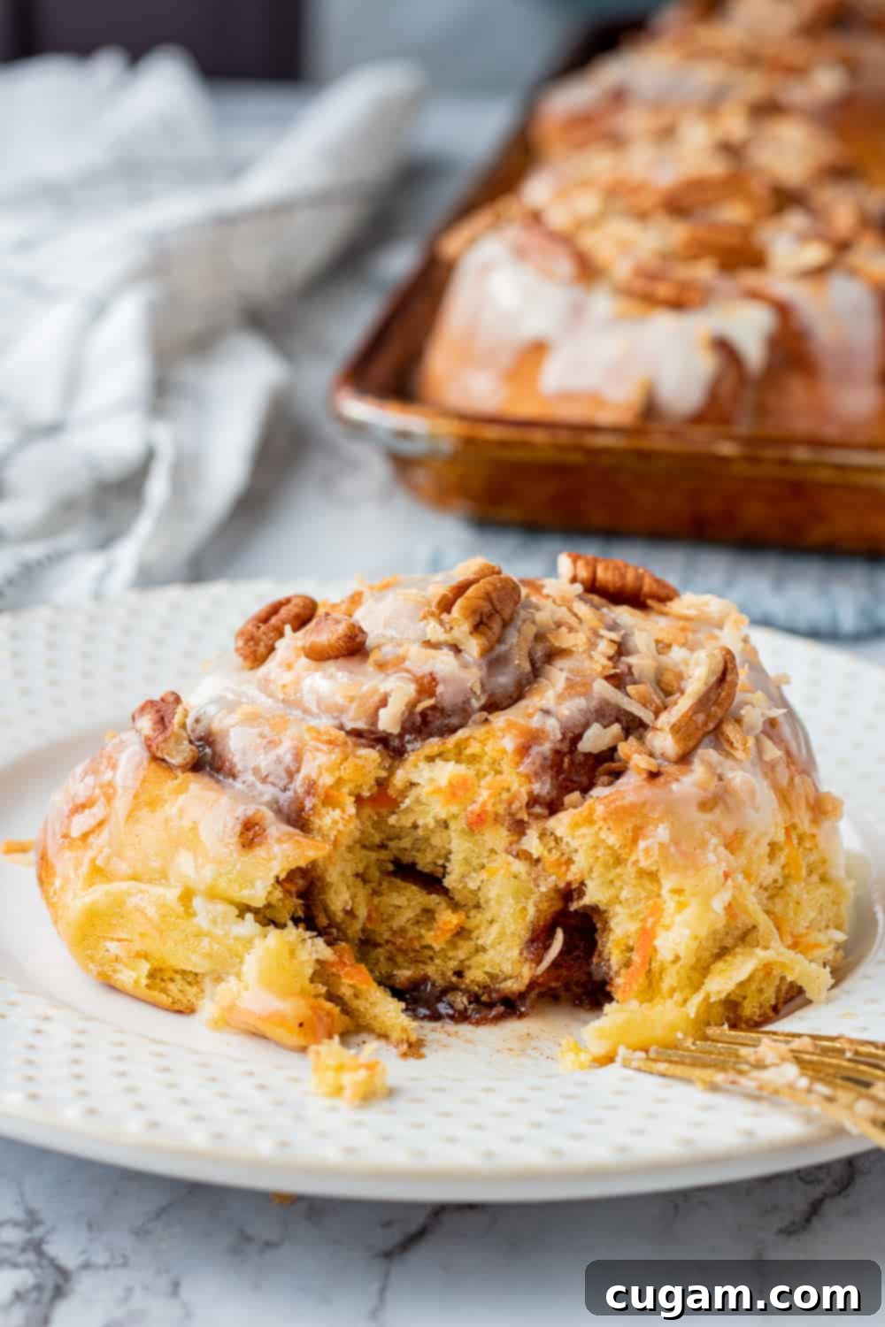 baked carrot cake cinnamon roll on white plate with gold fork on marble. 