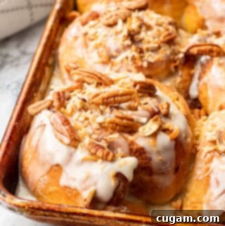 Carrot Cake Cinnamon Rolls 2 Baked carrot cake cinnamon roll with pecans and coconut on top in a metal pan on marble.