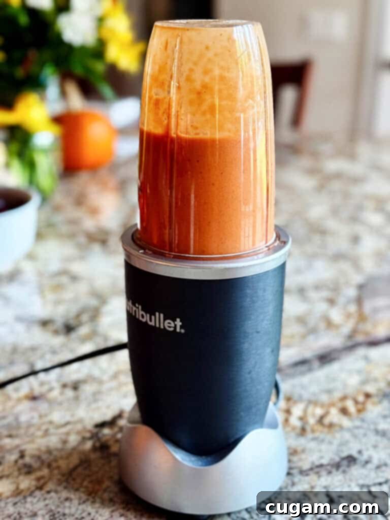 The blender puréeing roasted vegetables and broth into a smooth, creamy soup.