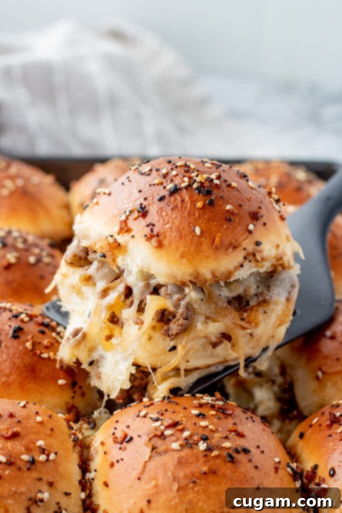 A delicious French Onion Ground Beef Slider, sliced in half, showing the rich ground beef and caramelized onion filling with melty cheese, resting on a black spatula. Perfect for game day! 