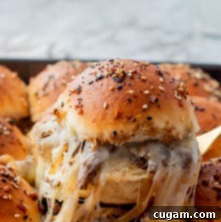 A French Onion Ground Beef Slider being lifted from a baking pan, showing the melty cheese and savory filling on a soft dinner roll.