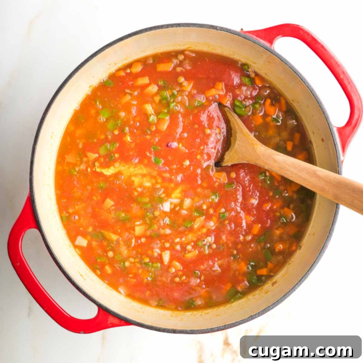 Veggies and lentils in a red tomato sauce, stirred with wooden spoon.