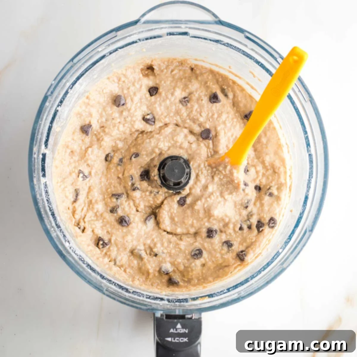 Spatula mixing chocolate chips into blondie batter in the bowl of a food processor. 