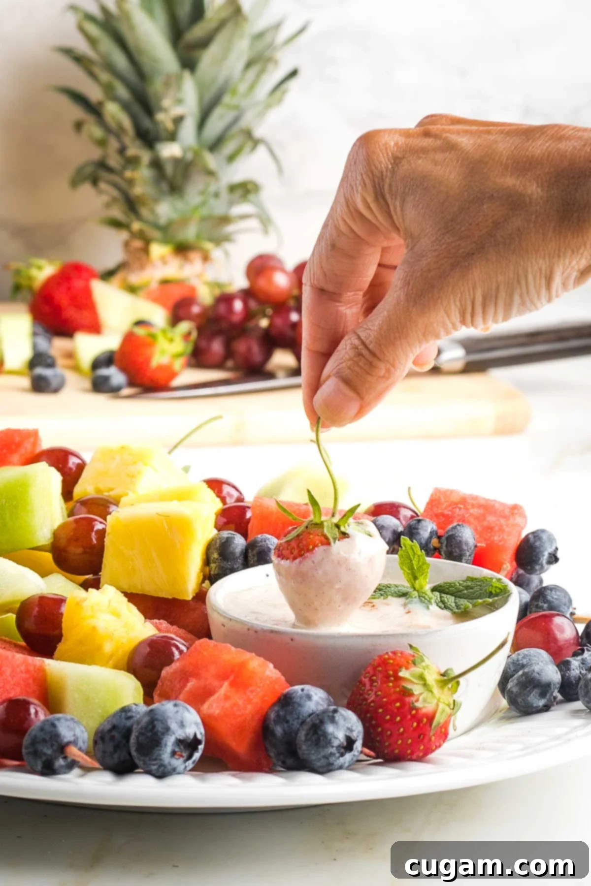 Strawberry coming out of fruit dip, on a platter of colorful assorted fruit skewers. 