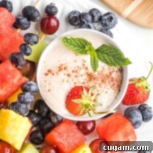Creamy dip with a sprinkle of cinnamon a strawberry and fresh mint sprig in a small bowl.