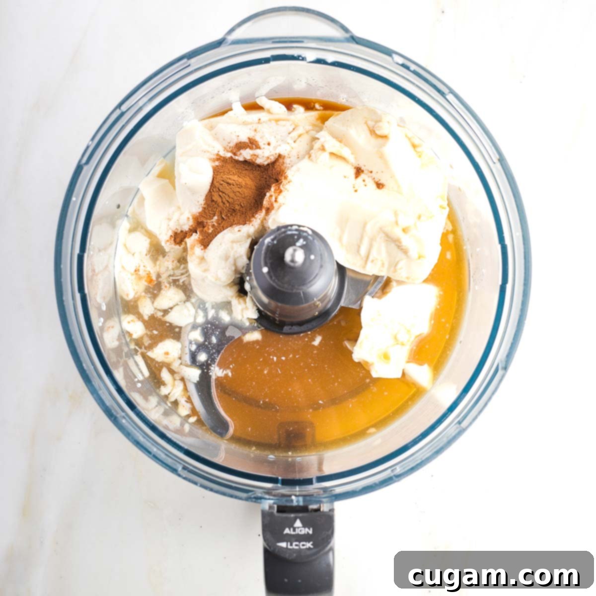 Fruit dip ingredients in the bowl of a food processor, including silken tofu, lemon juice, maple syrup, cinnamon and vanilla.