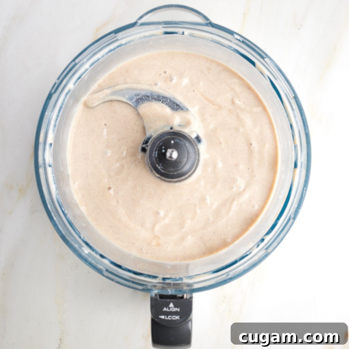 Beige creamy mixture in the bowl of a food processor.