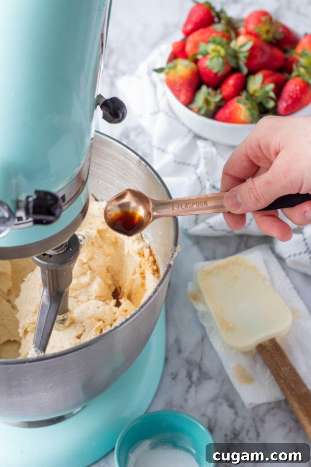 copper teaspoon with vanilla over metal bowl with raw pop tart cookie dough, blue mixer and strawberries in background. 