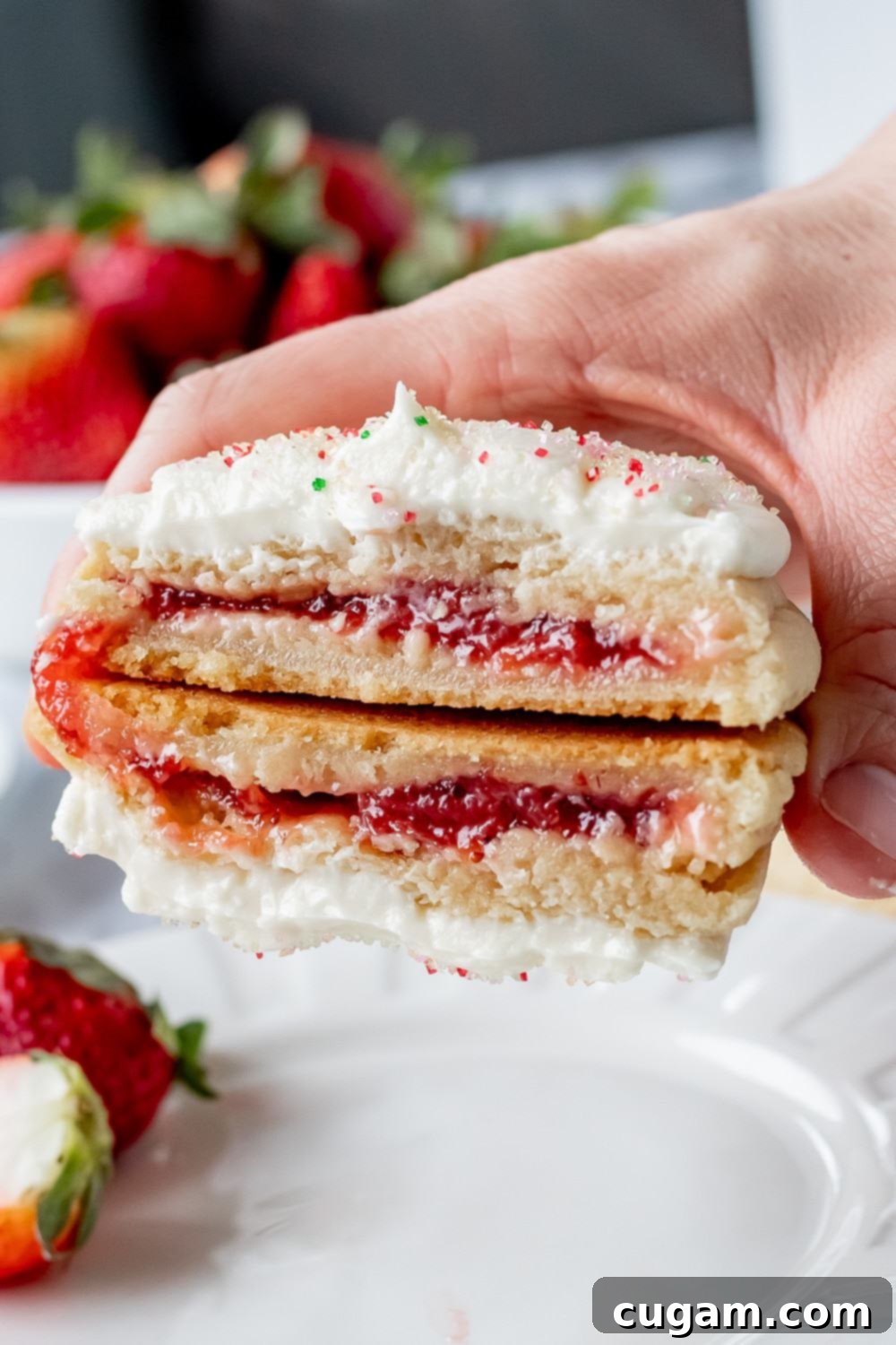 2 halves of strawberry pop tart cookie in a hand above a white plate with strawberries. 