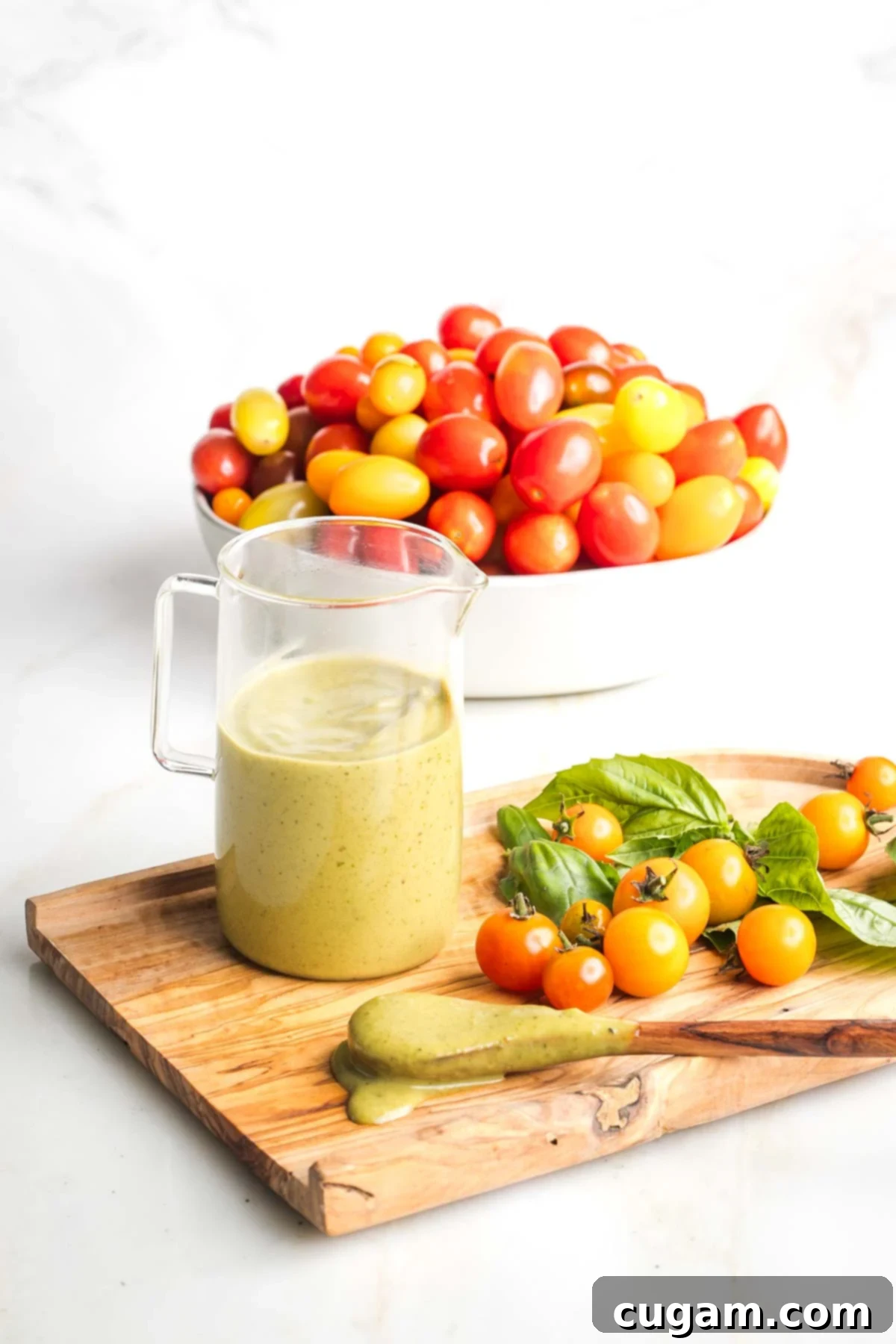 Creamy basil dressing in a small pitcher with colorful tomatoes in the background.