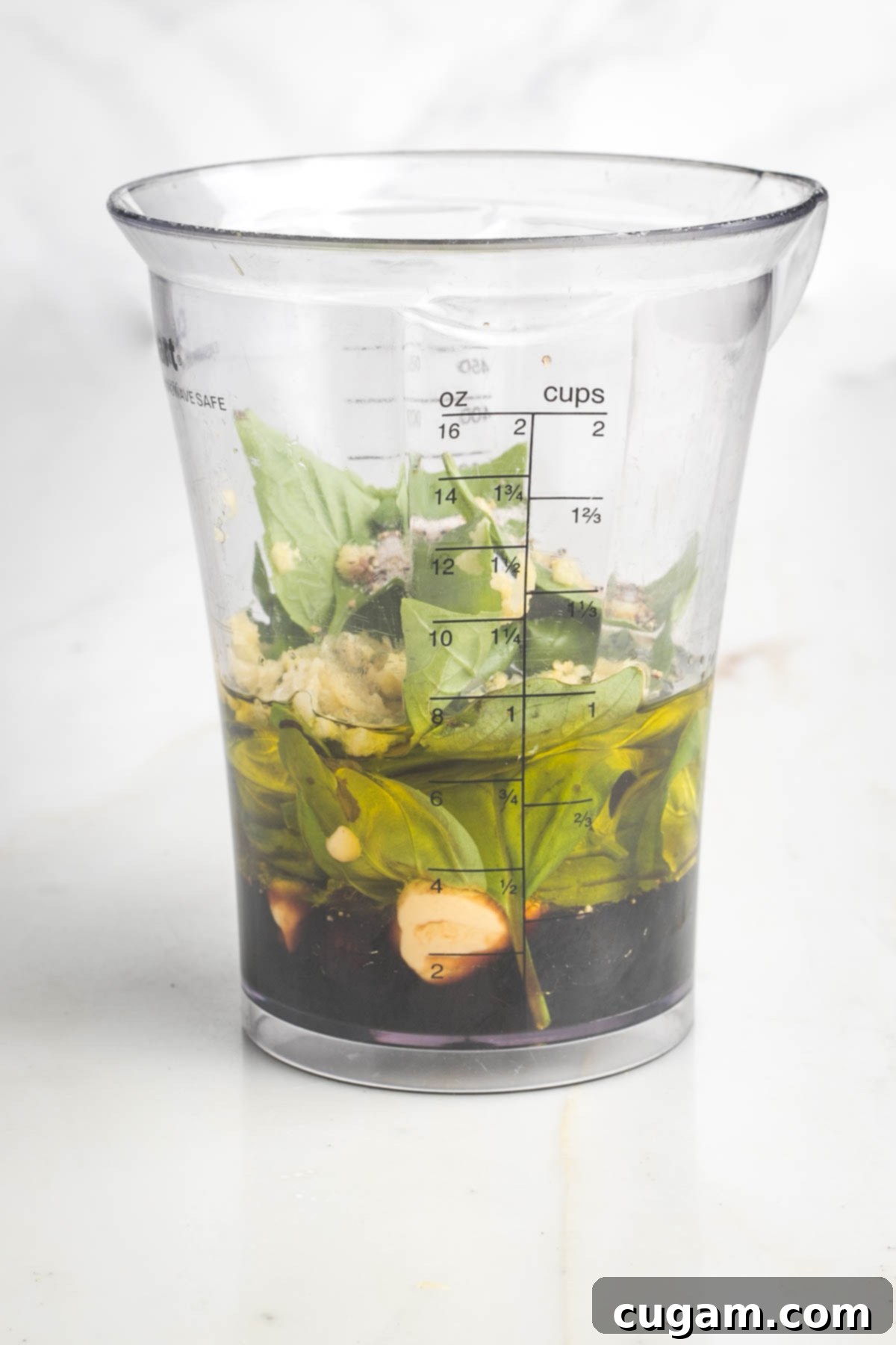 Fresh basil, balsamic vinegar, olive oil, mustard in a tall glass with marked measurements.