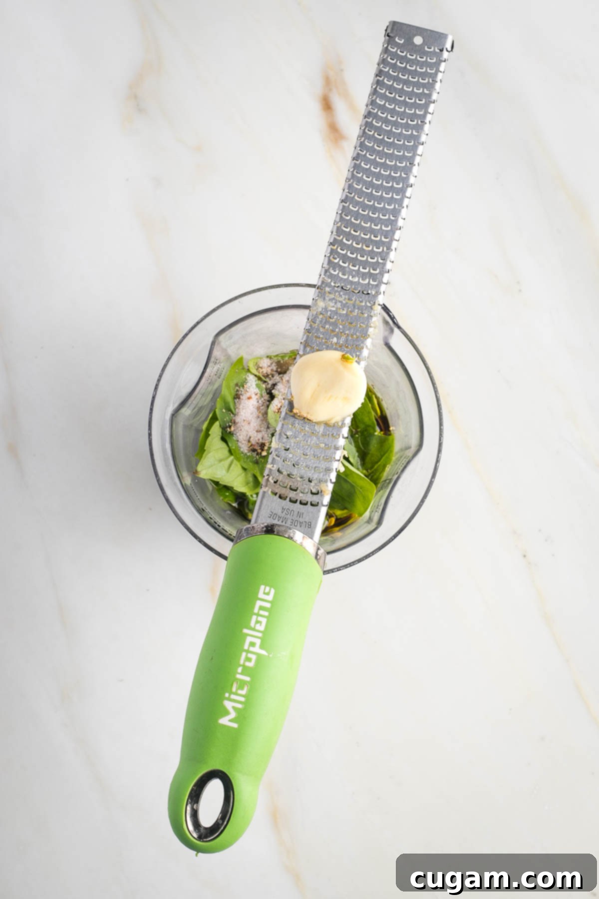 Microplane grater over a jar with fresh basil and other ingredients to make a dressing.