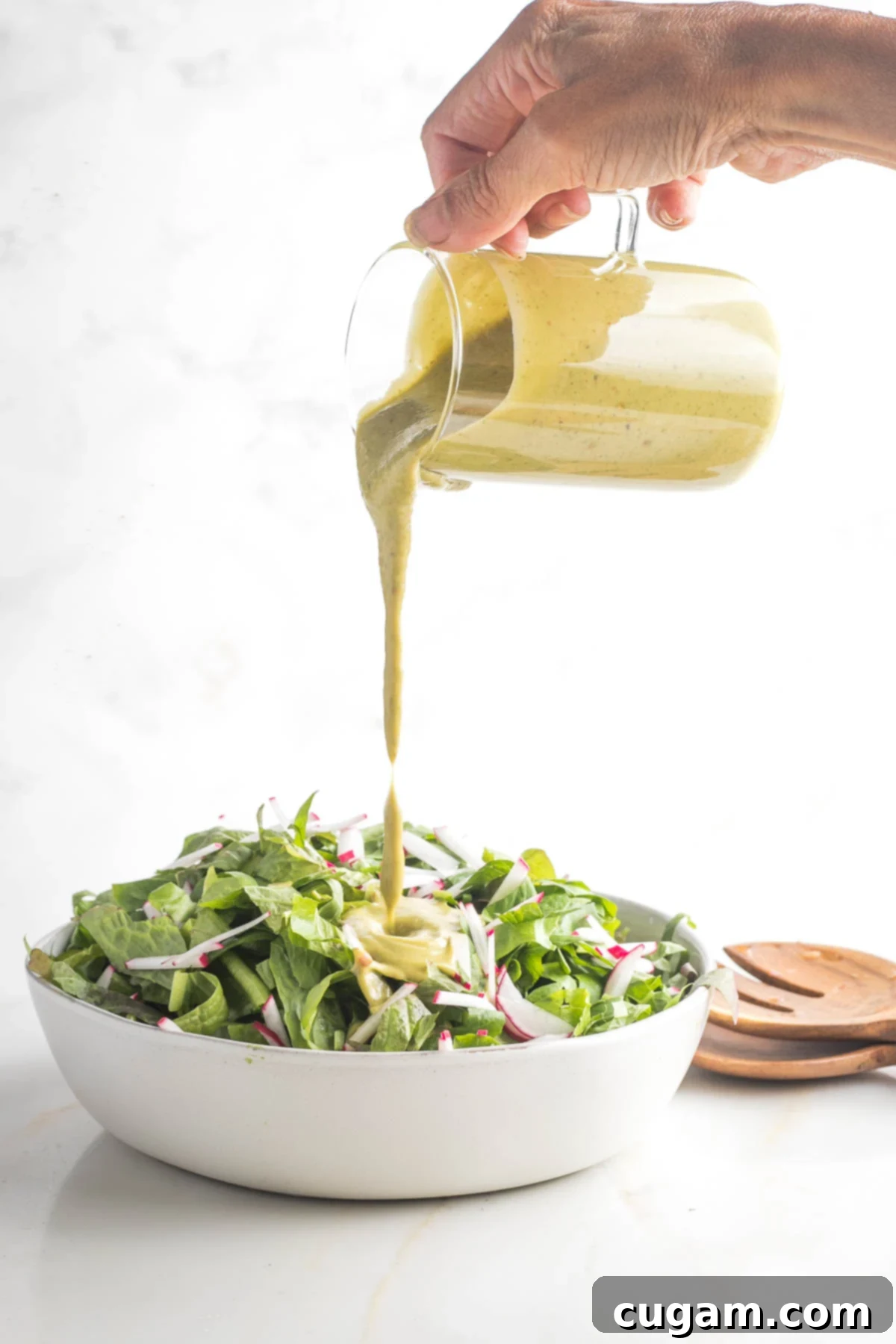 Thick and creamy basil balsamic vinaigrette pouring from glass pitcher onto salad greens.