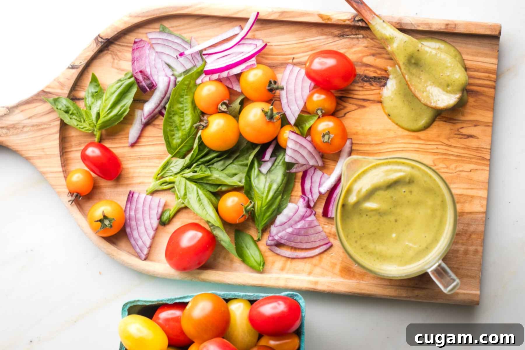 Bright orange and red cherry tomatoes, fresh basil and a pitcher plus wooden spoon with creamy dressing.