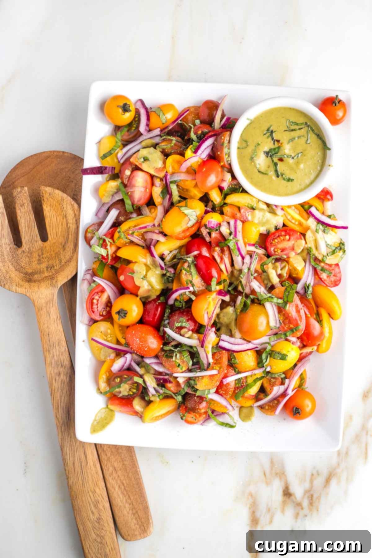 Bright and colorful chopped tomatoes, thinly sliced red onion, and fresh basil leaves artfully arranged on a white platter, with a small bowl of creamy balsamic dressing ready to be poured.