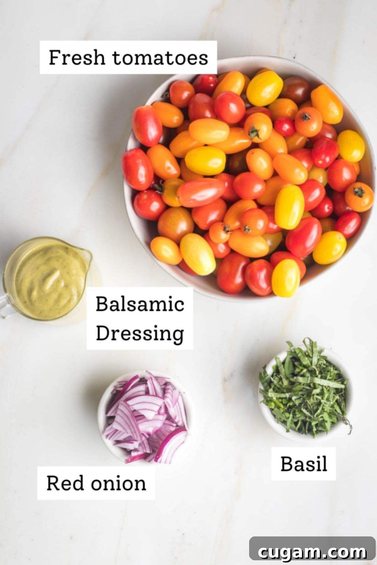 Individual bowls containing small whole tomatoes, julienned basil leaves, thinly sliced red onion, and a glass pitcher filled with creamy balsamic dressing, all arranged on a wooden surface.