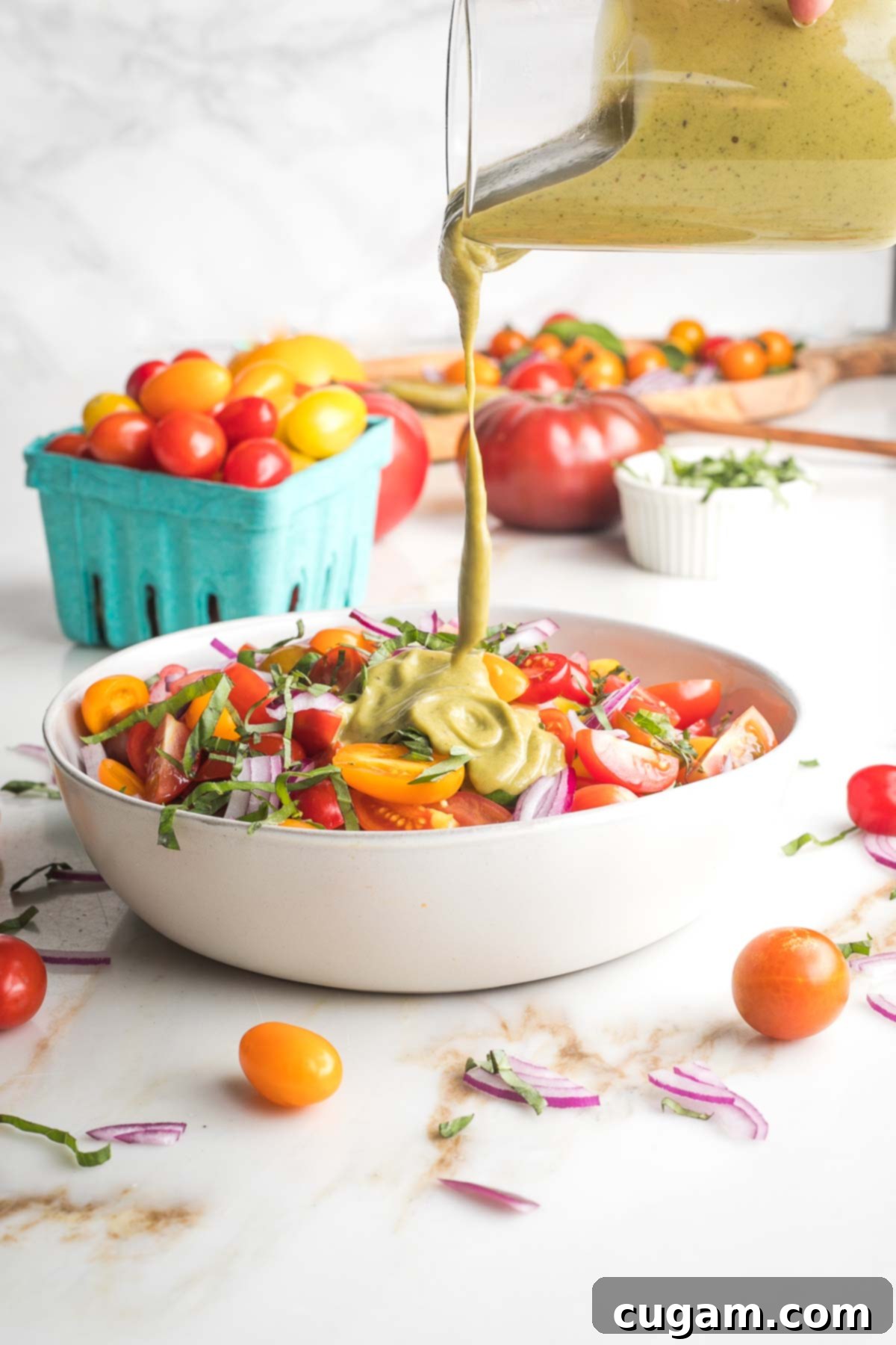 Creamy basil balsamic dressing being drizzled generously over a bowl filled with freshly chopped tomatoes, sliced onions, and aromatic basil, creating a visually appealing and flavorful mix.