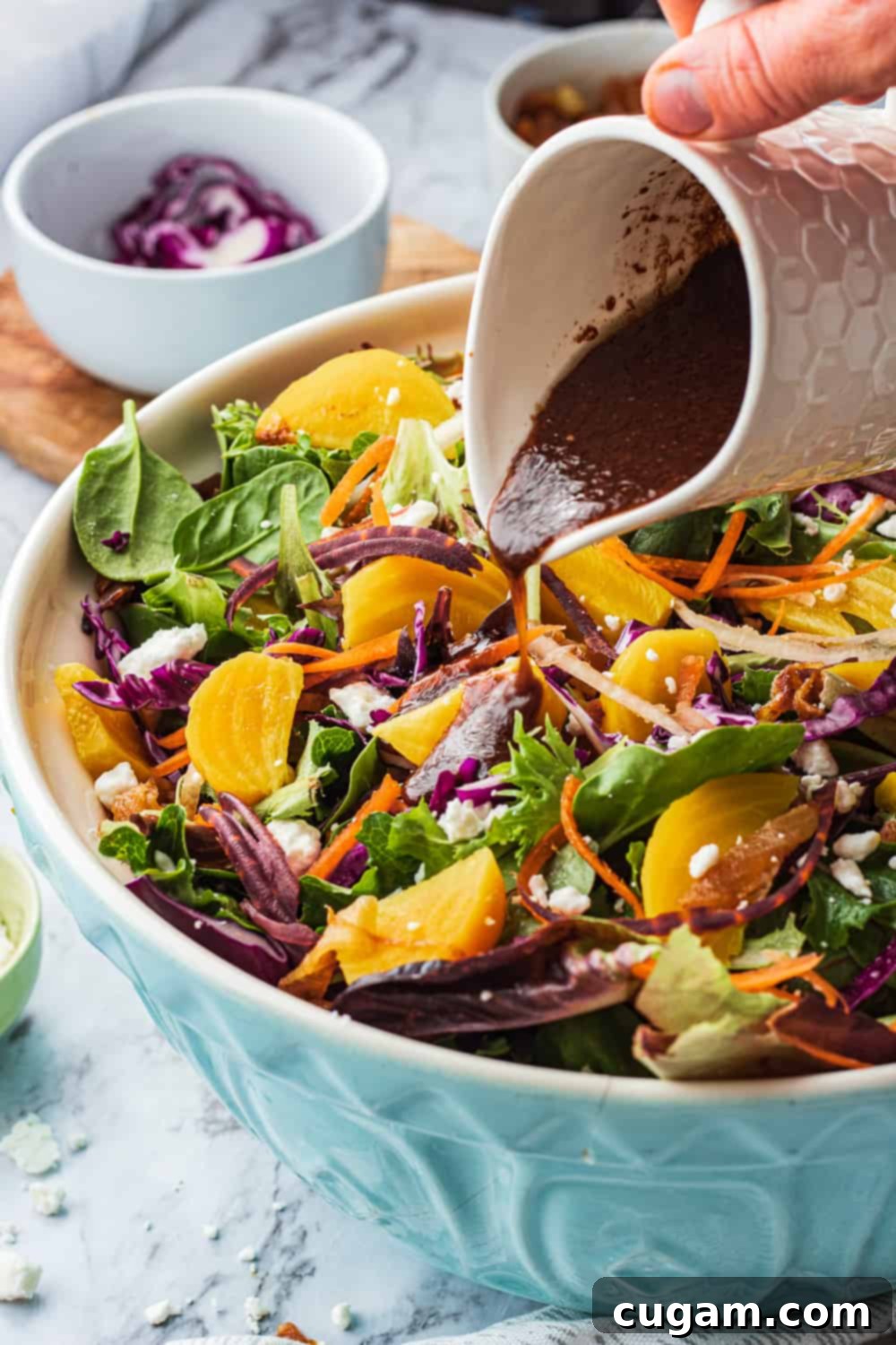 gold beets, red cabbage and carrots in a blue bowl with balsamic miso dressing pouring over salad. 