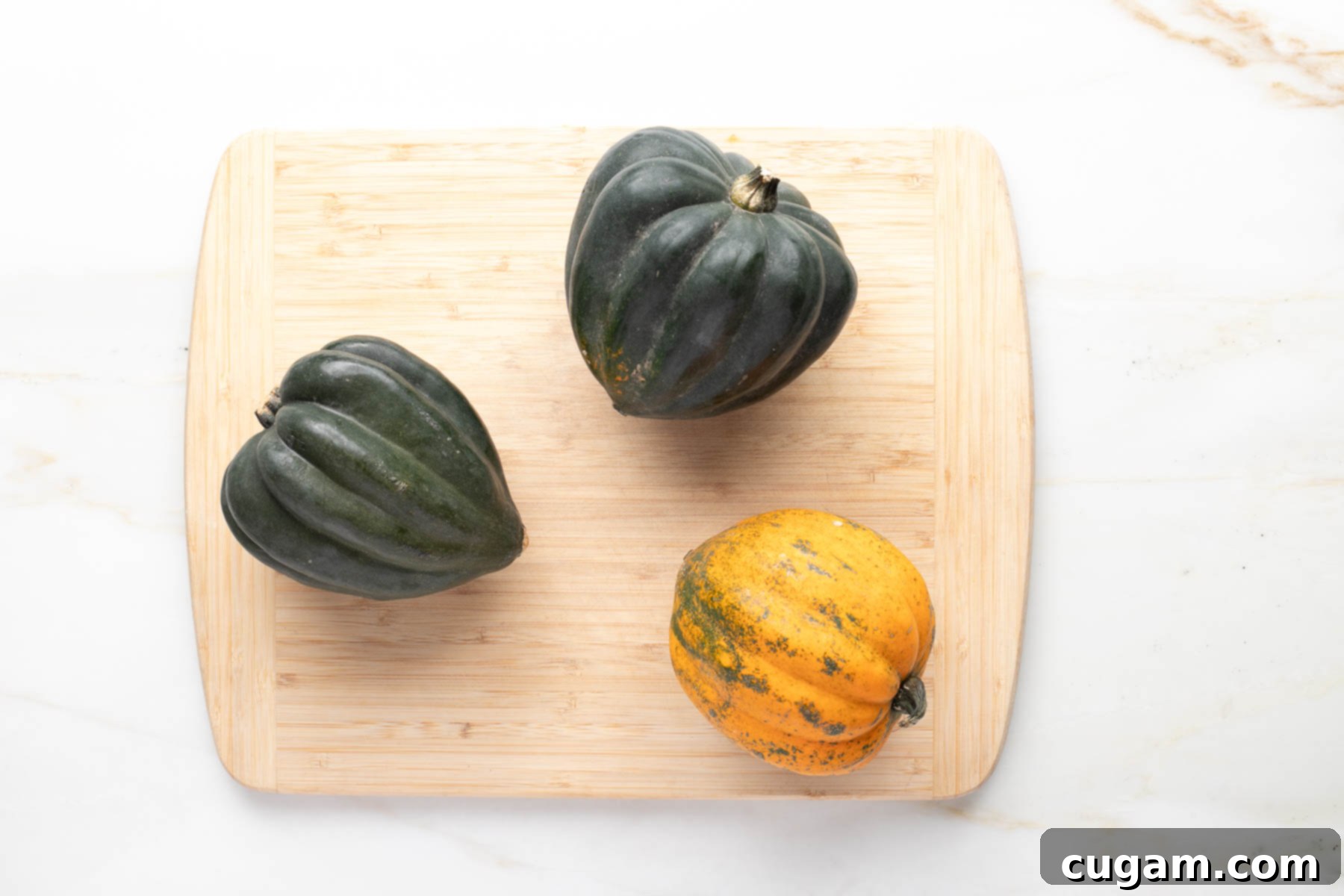 Three acorn squash on a cutting board. Two are green, one is speckled, mostly orange.