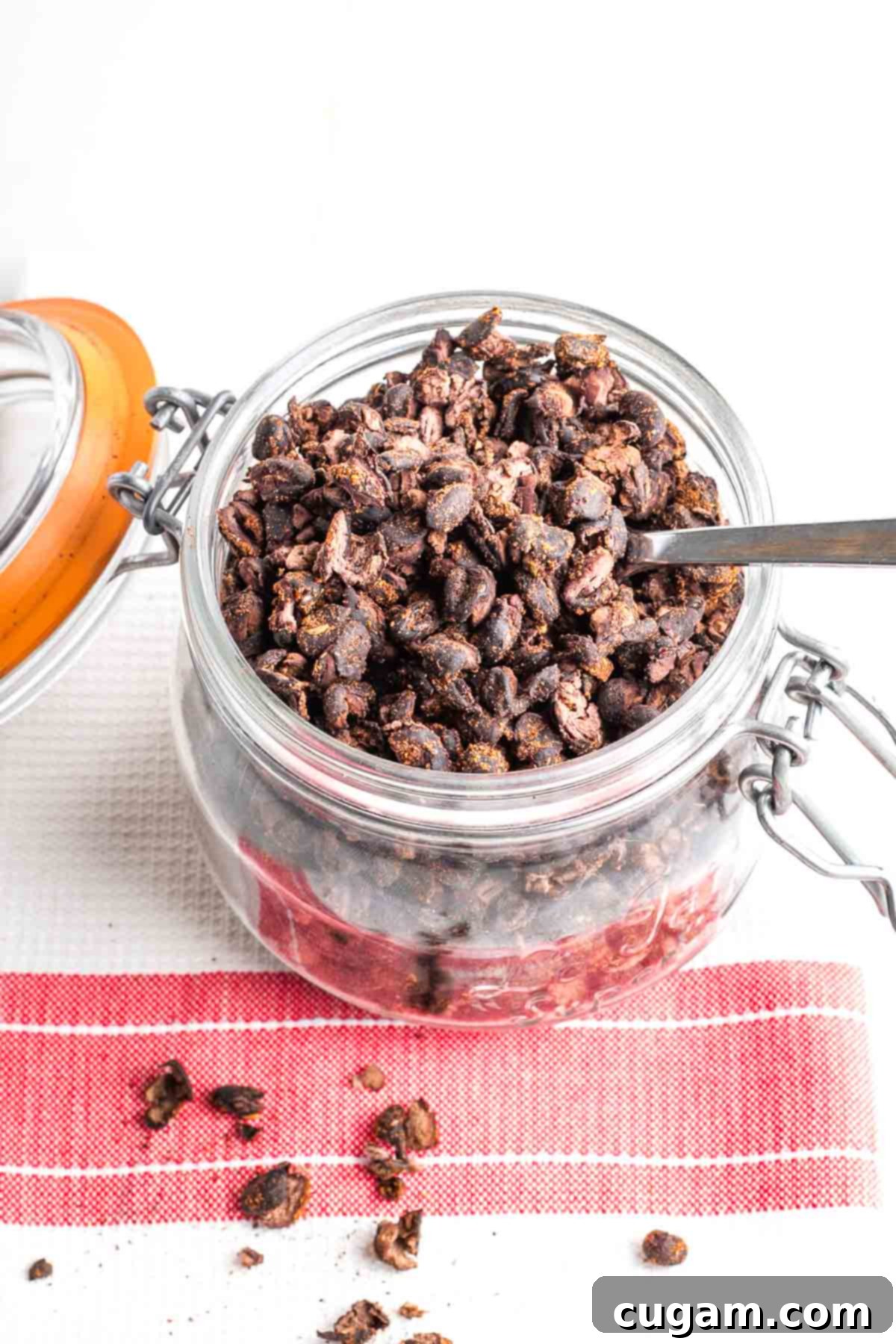 Lidded jar filled with crispy black beans, all on a tea towel with red stripe.