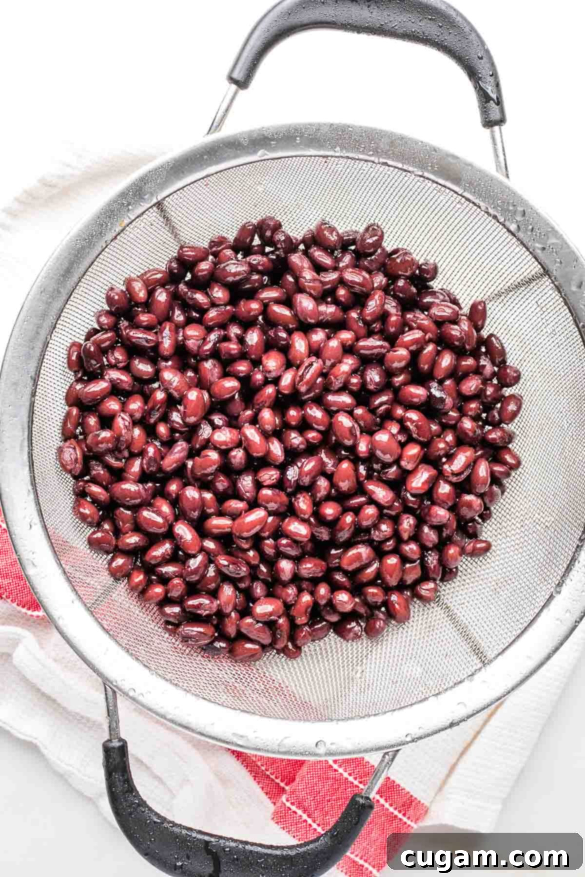 Mesh sieve filled with black beans and droplets of water.