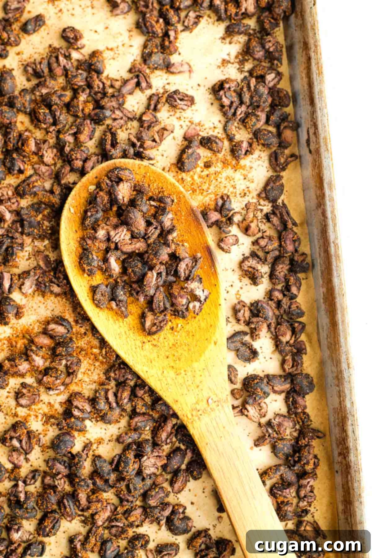 Wooden spoon showing close up of crispy black beans on a baking sheet.