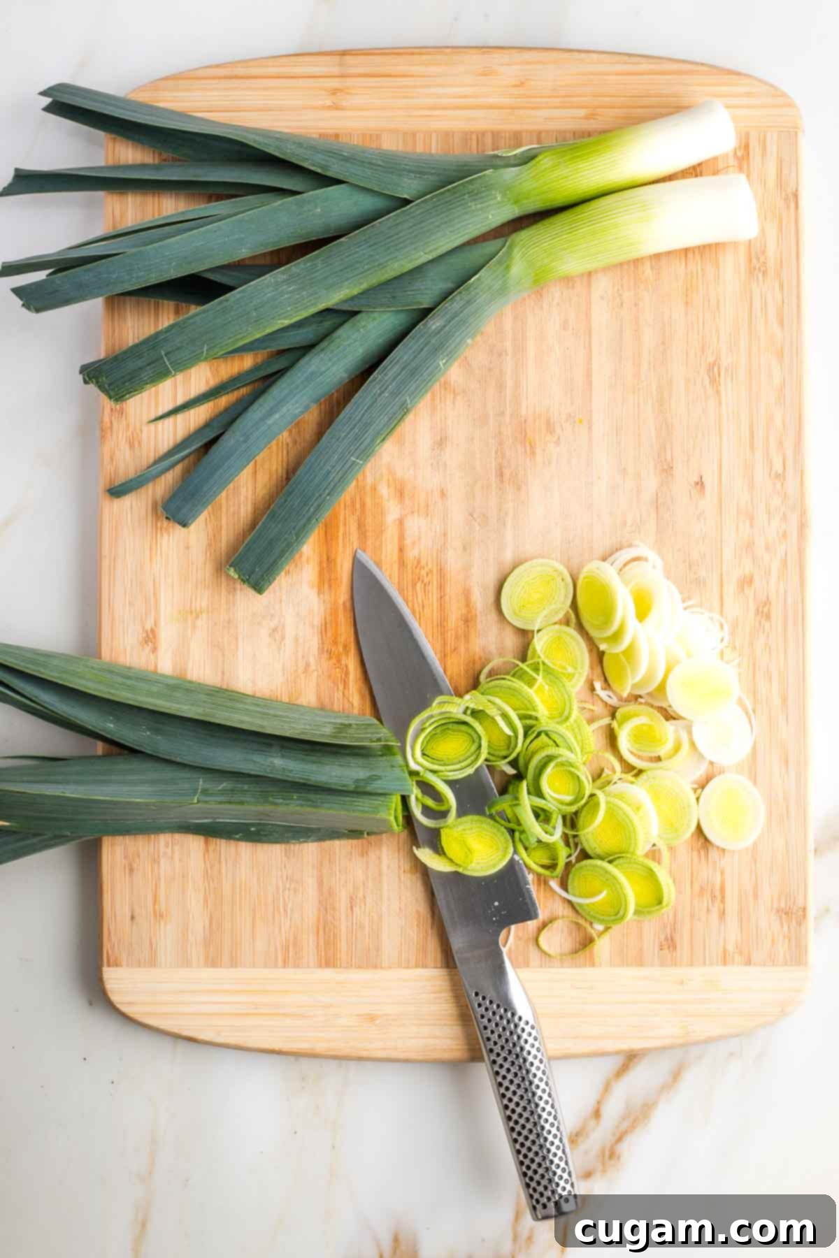 Leeks being thinly sliced on a cutting board, focusing on the white and light green sections of the leek.