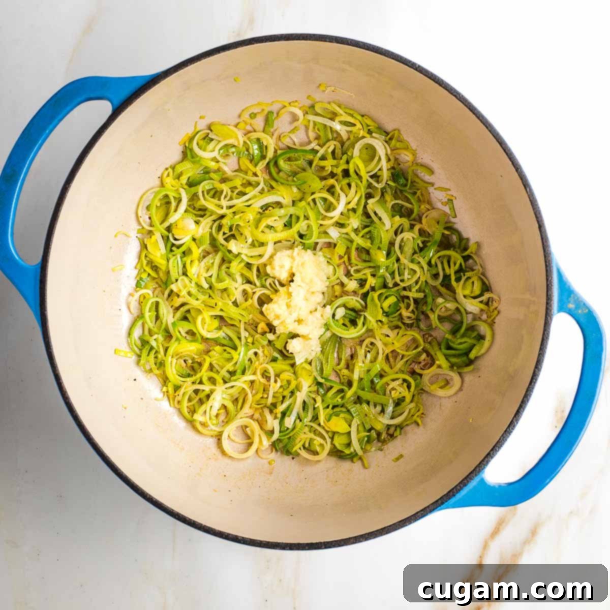 Sauteed leeks in a dutch oven with a pile of pressed garlic in the center.