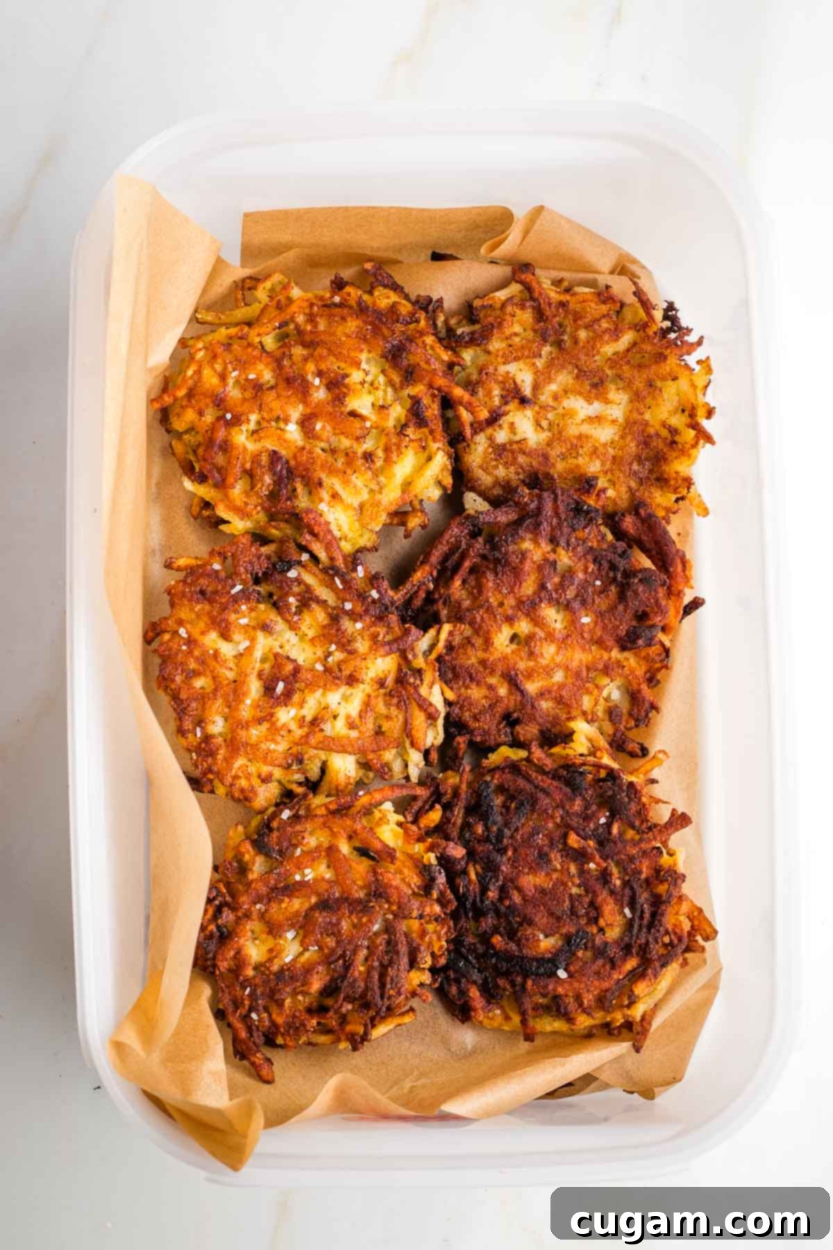Grandma's Secret Potato Latkes 17 Large tupperware filled with layers of latkes separated by sheets of parchment paper.