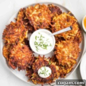 Grandma's Secret Potato Latkes 18 Crispy potato latkes on a platter with a small dish of sour cream in the center.